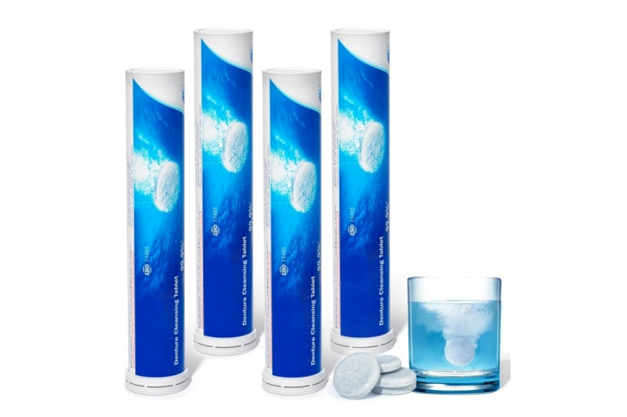 Blue-and-white denture tablet tubes beside tablets and a glass